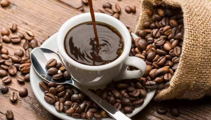 Filling a cup of coffee on a wooden table, with a burlap sack and coffee beans